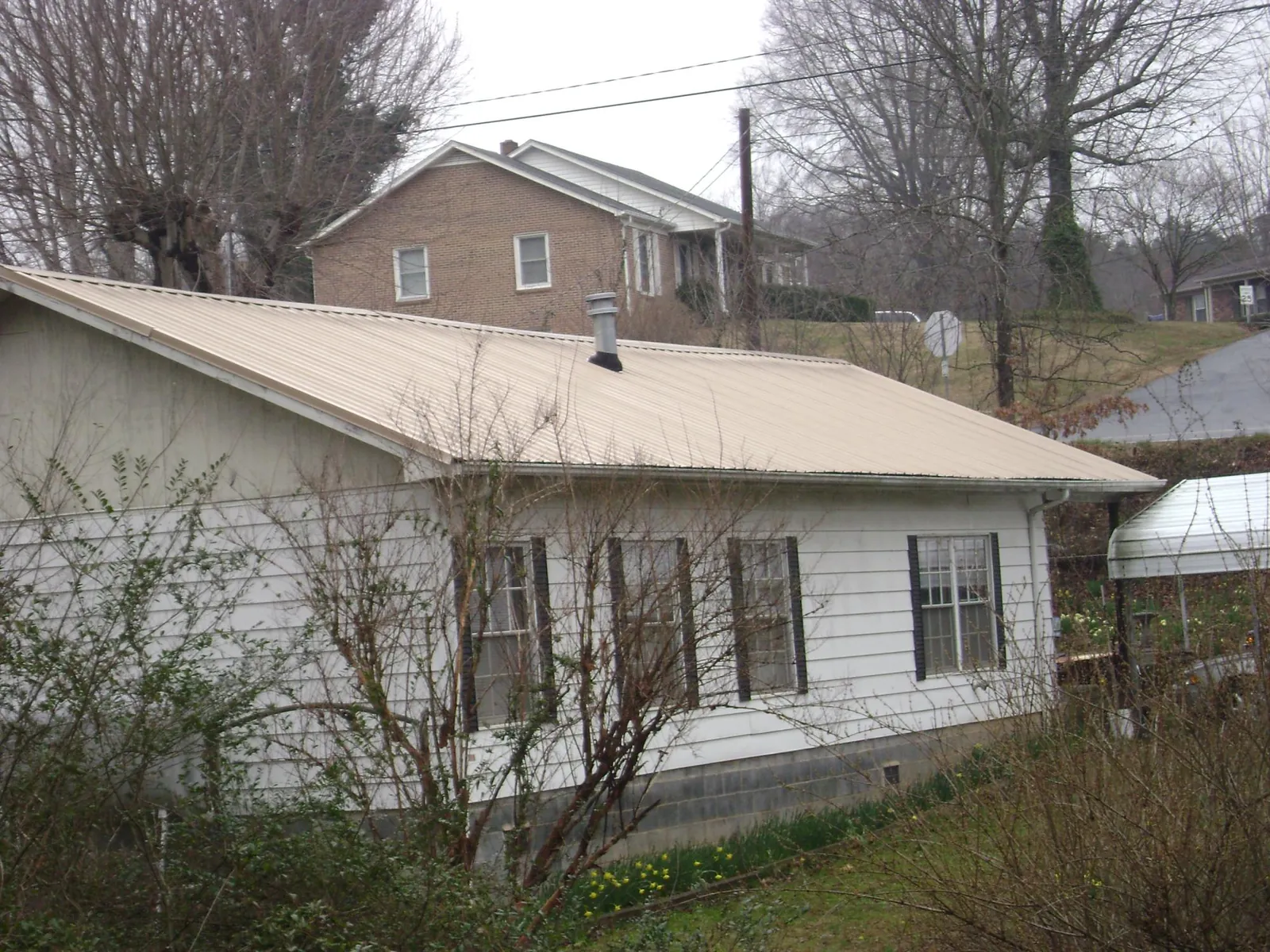Tan metal roof on a white sided house set into a hillside — Commercial Roofing by Roofing Brothers in Middletown
